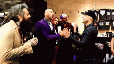 A Group Of Men Are Standing In A Room Talking To Each Other . One Of The Men Is Wearing A Purple Suit . GIF