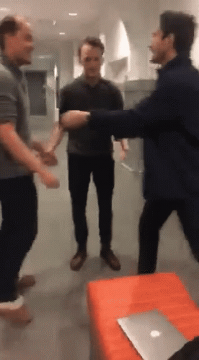 A Group Of Men Are Standing In A Room With A Laptop On The Table GIF