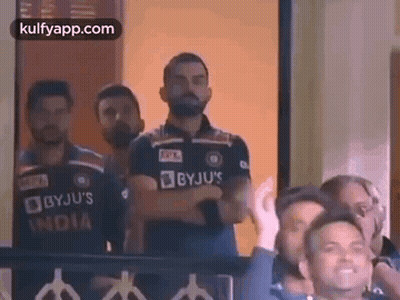 A Group Of Men Are Standing In A Room With Their Arms Crossed And Watching A Cricket Match . GIF
