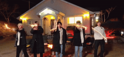 A Group Of Men Are Standing In Front Of A House Holding Sparklers . GIF
