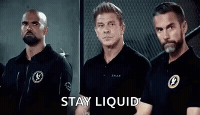 A Group Of Men Are Standing Next To Each Other In A Room With The Words `` Stay Liquid '' Written On The Screen . GIF