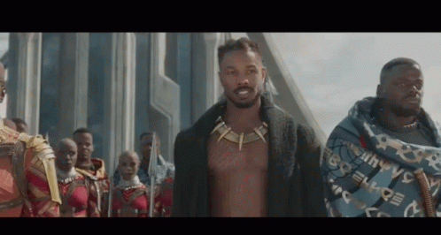 A Group Of Men Are Standing Next To Each Other In Front Of A Building . One Of The Men Is Without A Shirt On . GIF