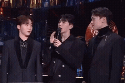 A Group Of Men Are Standing Next To Each Other On A Stage Singing Into Microphones . GIF