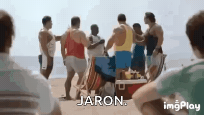 A Group Of Men Are Standing On A Beach Talking To Each Other And Jaron Is Standing In The Middle Of The Group . GIF