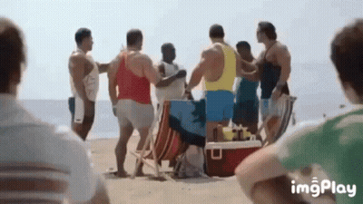 A Group Of Men Are Standing On A Beach With A Red Cooler . GIF