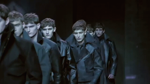A Group Of Men Are Walking Down A Runway In A Line . GIF