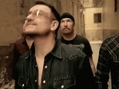 A Group Of Men Are Walking Down A Street . One Of The Men Is Wearing Glasses . GIF