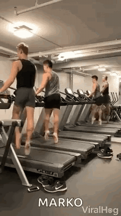 A Group Of Men Are Walking On Treadmills In A Gym . GIF