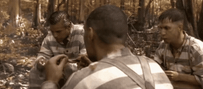 A Group Of Men In Striped Shirts Are Sitting In A Forest GIF