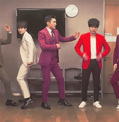 A Group Of Men In Suits And Jackets Are Dancing In Front Of A Clock GIF