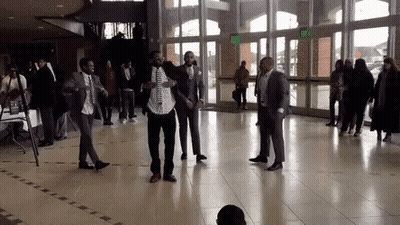 A Group Of Men In Suits And Ties Are Dancing In A Large Hallway . GIF