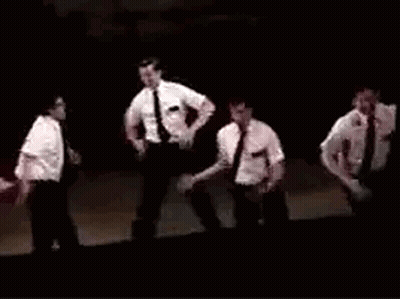 A Group Of Men In Suits And Ties Are Dancing On A Stage In A Dark Room . GIF
