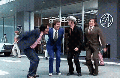 A Group Of Men In Suits And Ties Are Dancing On The Sidewalk In Front Of A Store . GIF