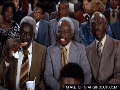 A Group Of Men In Suits And Ties Are Sitting In A Crowd And One Of Them Is Eating A Slice Of Pizza GIF