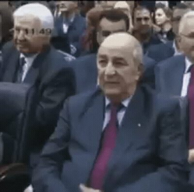 A Group Of Men In Suits And Ties Are Sitting In A Row In A Room . GIF