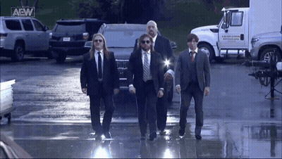 A Group Of Men In Suits And Ties Are Walking In Front Of A Truck That Says Aew On It GIF