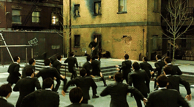 A Group Of Men In Suits Are Dancing In Front Of A Brick Building That Has Graffiti On It That Says ' Ec ' GIF