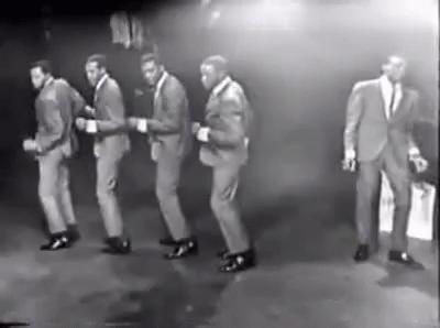 A Group Of Men In Suits Are Dancing Together On A Stage . GIF