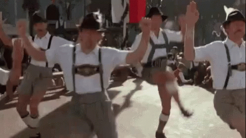 A Group Of Men In Traditional German Clothing Are Dancing Together . GIF