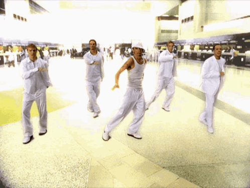 A Group Of Men In White Are Dancing In A Hallway GIF