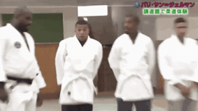 A Group Of Men In White Karate Uniforms Are Standing Next To Each Other . GIF