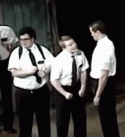 A Group Of Men In White Shirts And Black Ties Are Standing In A Dark Room GIF