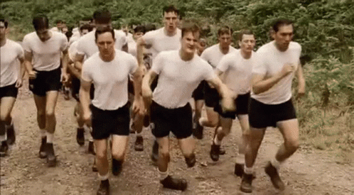 A Group Of Men In White Shirts And Shorts Are Running Down A Dirt Road . GIF