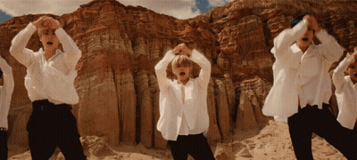 A Group Of Men In White Shirts Are Dancing In Front Of A Rocky Mountain GIF