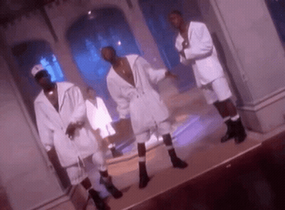 A Group Of Men In White Suits And Socks Are Dancing On A Stage In A Room . GIF