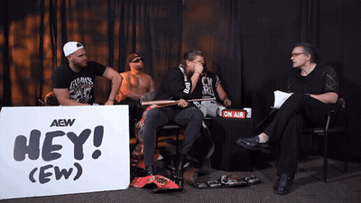 A Group Of Men Sitting In Front Of A Sign That Says Hey GIF