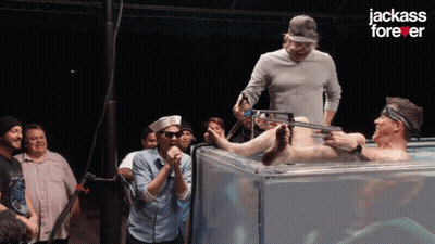 A Group Of Men Standing Around A Man In A Tank With The Words Jackass Forever On The Bottom GIF