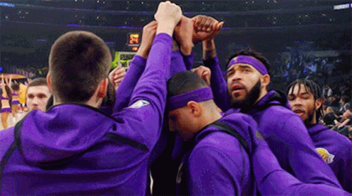 A Group Of Men Wearing Purple Sweatshirts And Headbands Are Huddled Together . GIF