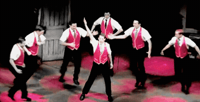 A Group Of Men Wearing Red Vests And White Shirts Are Dancing On A Stage GIF