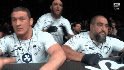 A Group Of Men Wearing White Ufc Shirts Are Watching A Fight GIF