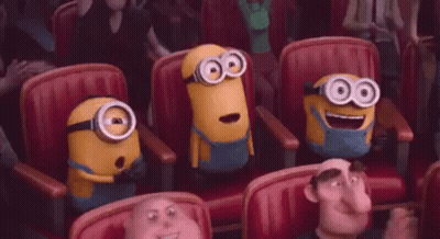 a group of minions are sitting in a row of red chairs in a theater .