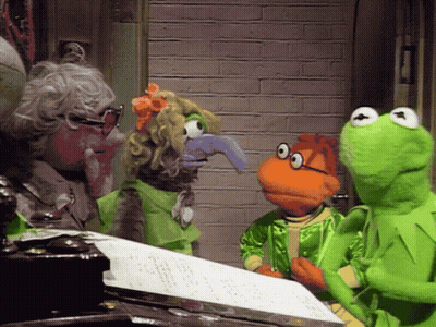 A Group Of Muppets Including Kermit The Frog Are Standing Around A Sheet Of Paper GIF