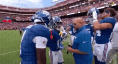 A Group Of New York Giants Football Players Are Standing On A Field Talking To Each Other . GIF