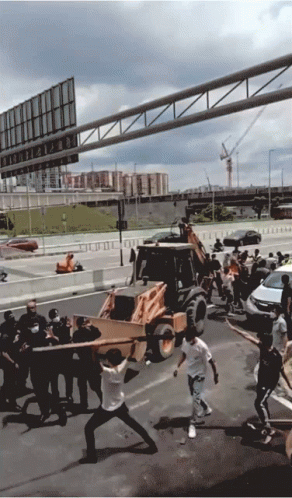 A Group Of People Are Carrying A Large Piece Of Wood In Front Of A Bulldozer On A Highway GIF