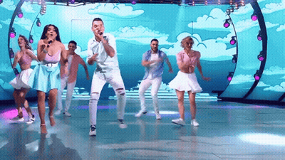 A Group Of People Are Dancing And Singing On A Stage With A Blue Background GIF