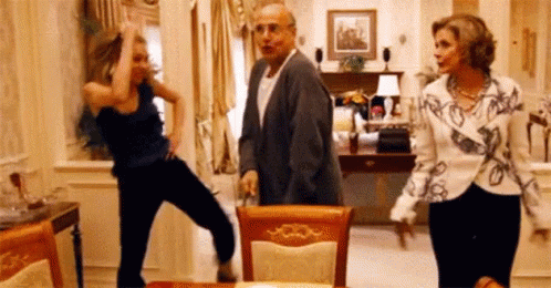A Group Of People Are Dancing In A Living Room In Front Of A Table . GIF
