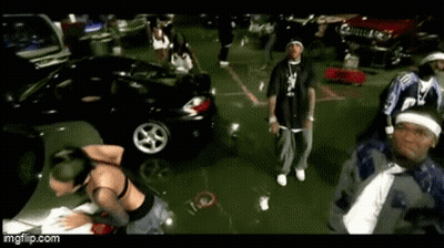 A Group Of People Are Dancing In A Parking Lot With Cars In The Background . GIF