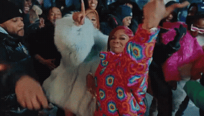 A Group Of People Are Dancing In A Room With A Woman Wearing A Colorful Jacket . GIF