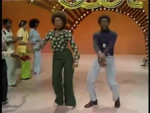A Group Of People Are Dancing In Front Of A Carnival Arch GIF