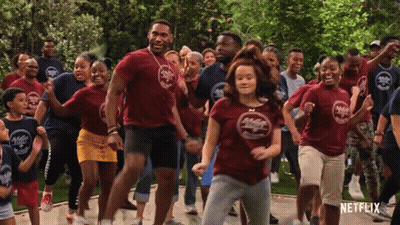 A Group Of People Are Dancing In Front Of A Sign That Says Netflix On It GIF