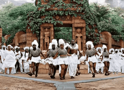 A Group Of People Are Dancing In Front Of A Statue . GIF