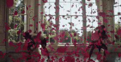 A Group Of People Are Dancing In Front Of A Window With Petals Falling On The Floor GIF