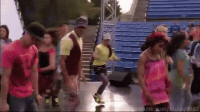 A Group Of People Are Dancing In Front Of Blue Bleachers With Youtube.com In The Bottom Right Corner GIF