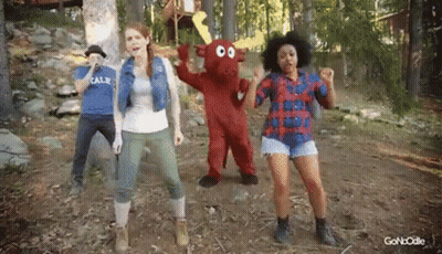 A Group Of People Are Dancing In The Woods With A Mascot In The Middle . GIF