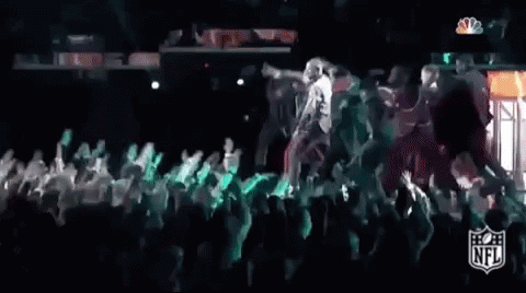 A Group Of People Are Dancing On A Stage In Front Of A Crowd At A Football Game . GIF