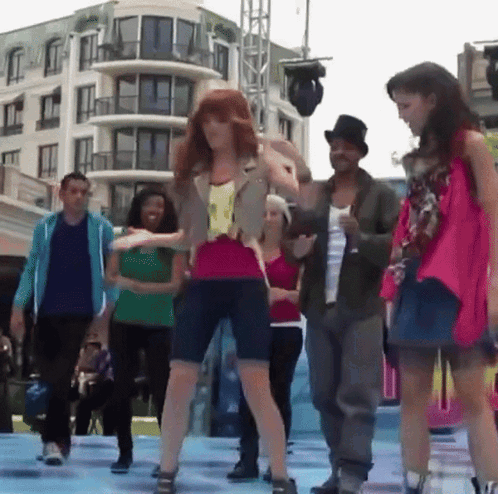 A Group Of People Are Dancing On A Stage In Front Of A Large Building GIF